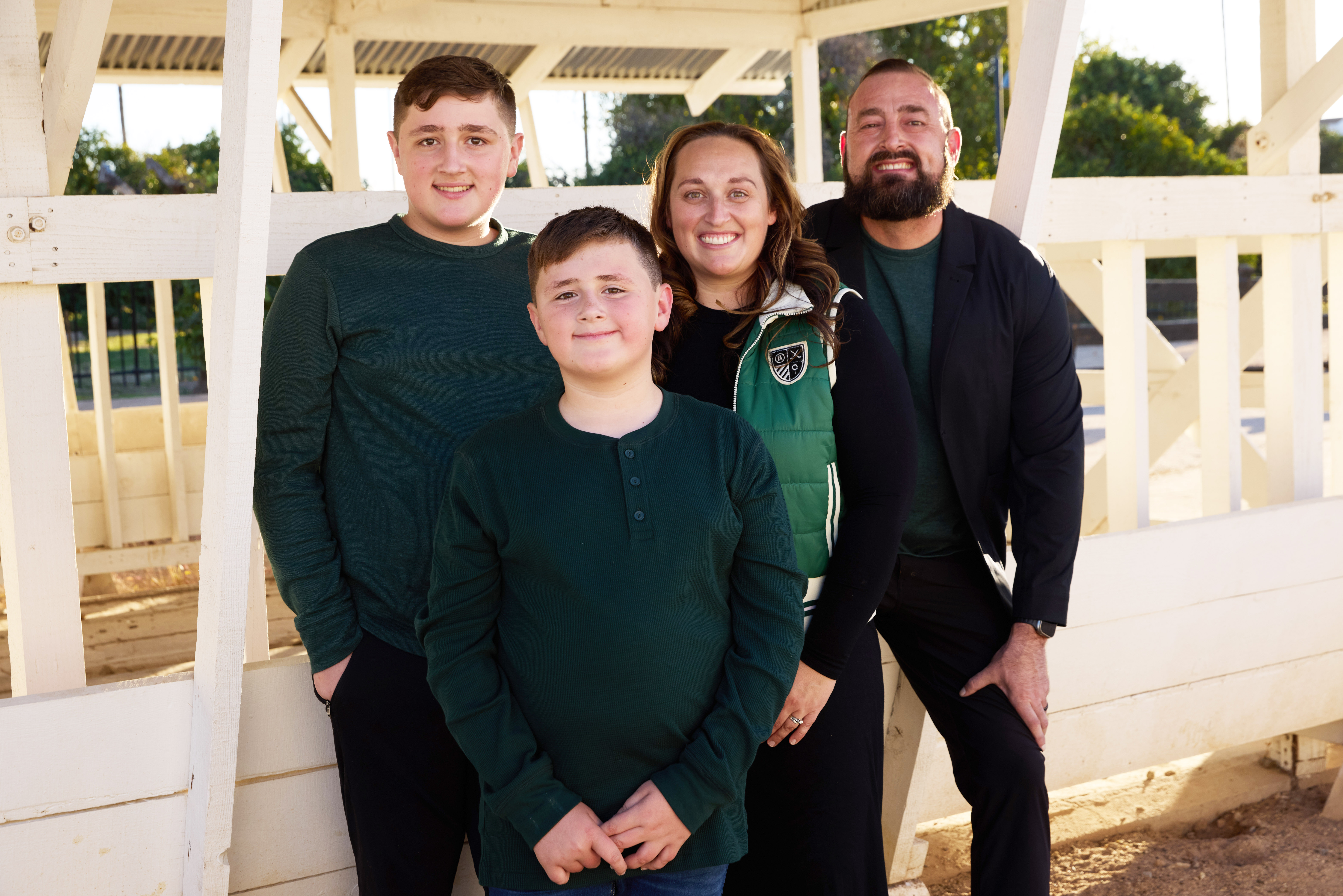 Family of four smiling in front of a white wooden gazebo structure at Sahuaro Ranch Park.